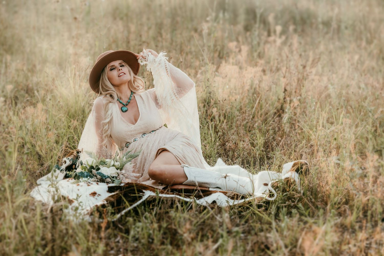 A dreamy outdoor portrait on a vintage blanket in a sunlit meadow with tall grass and boho styling.