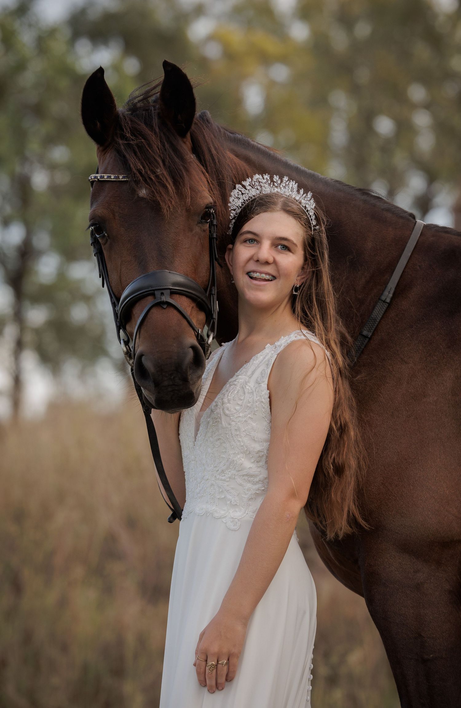 A white dress and tiara create an elegant portrait with a dark bay horse in natural lighting.