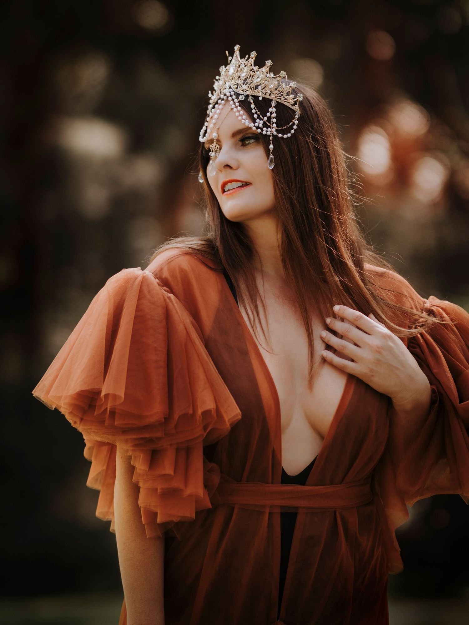 Dramatic rust-colored dress with statement sleeves and ornate crystal crown headpiece in moody forest setting.