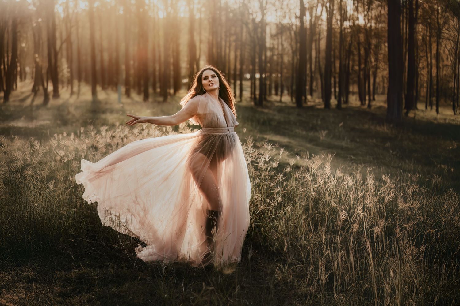 A flowing pink dress twirls gracefully in a sunlit forest during golden hour creating an ethereal scene.