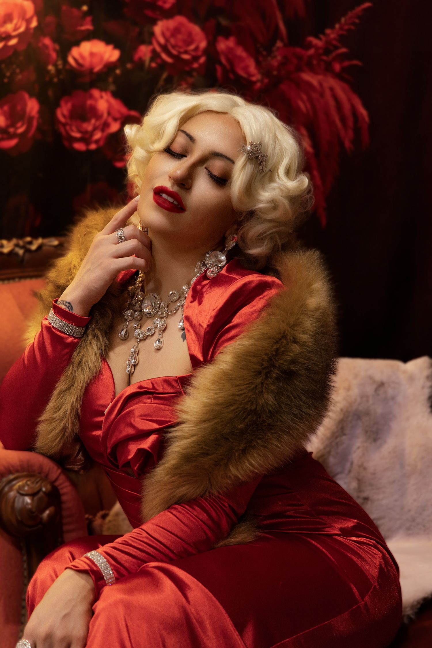 Glamorous vintage-inspired photoshoot featuring red satin dress and fur stole against dark floral backdrop.