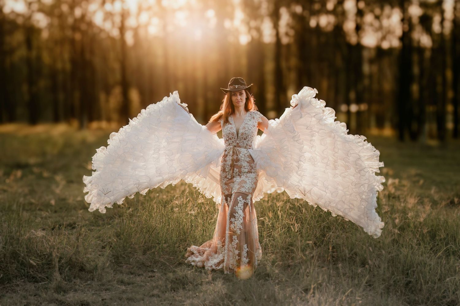 A person in a flowy white dress stands in a sunlit forest during golden hour, creating a dreamy ethereal scene.