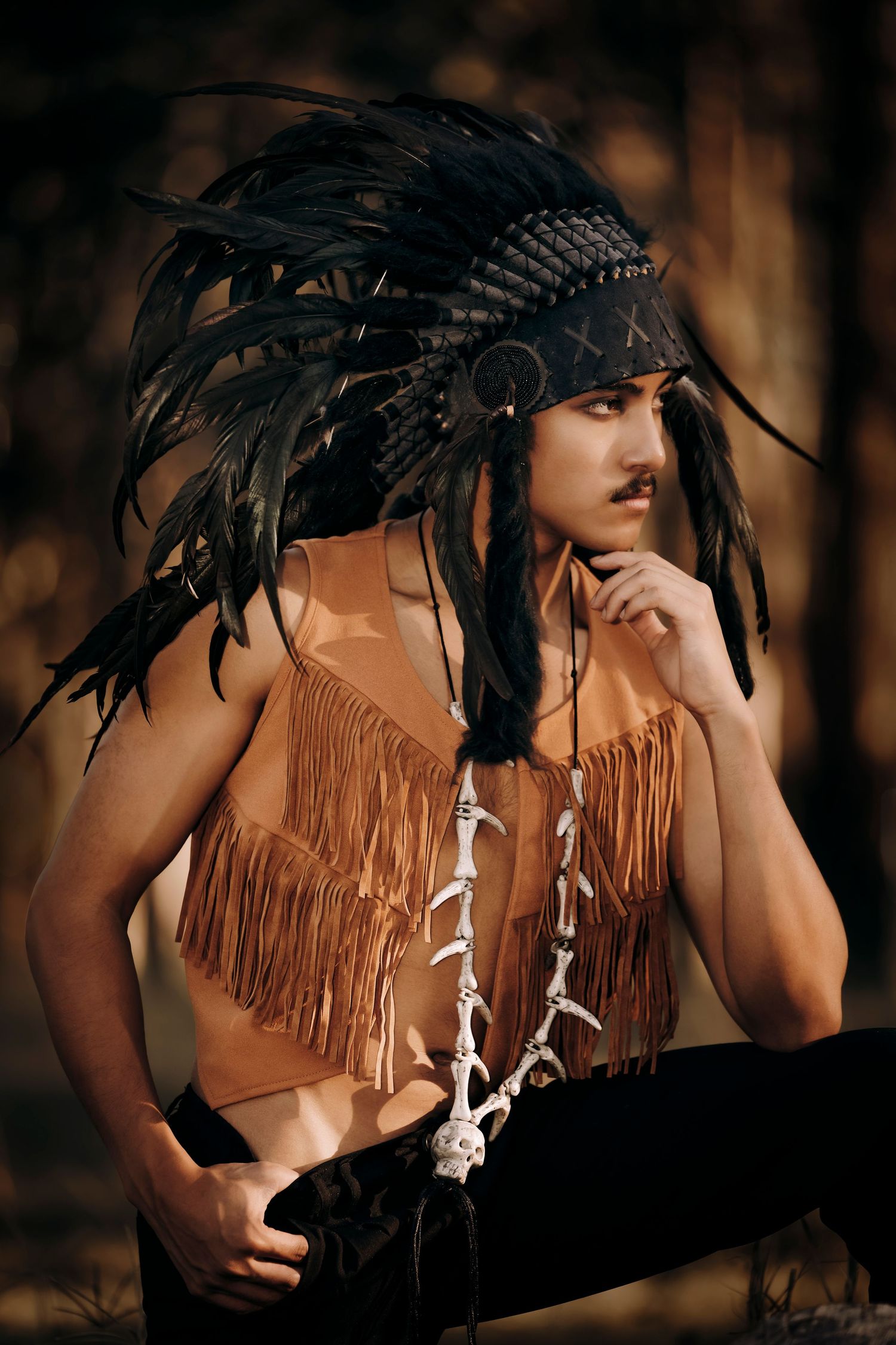 A Native American-inspired costume featuring black feather headdress and tan fringed top in a moody forest setting.