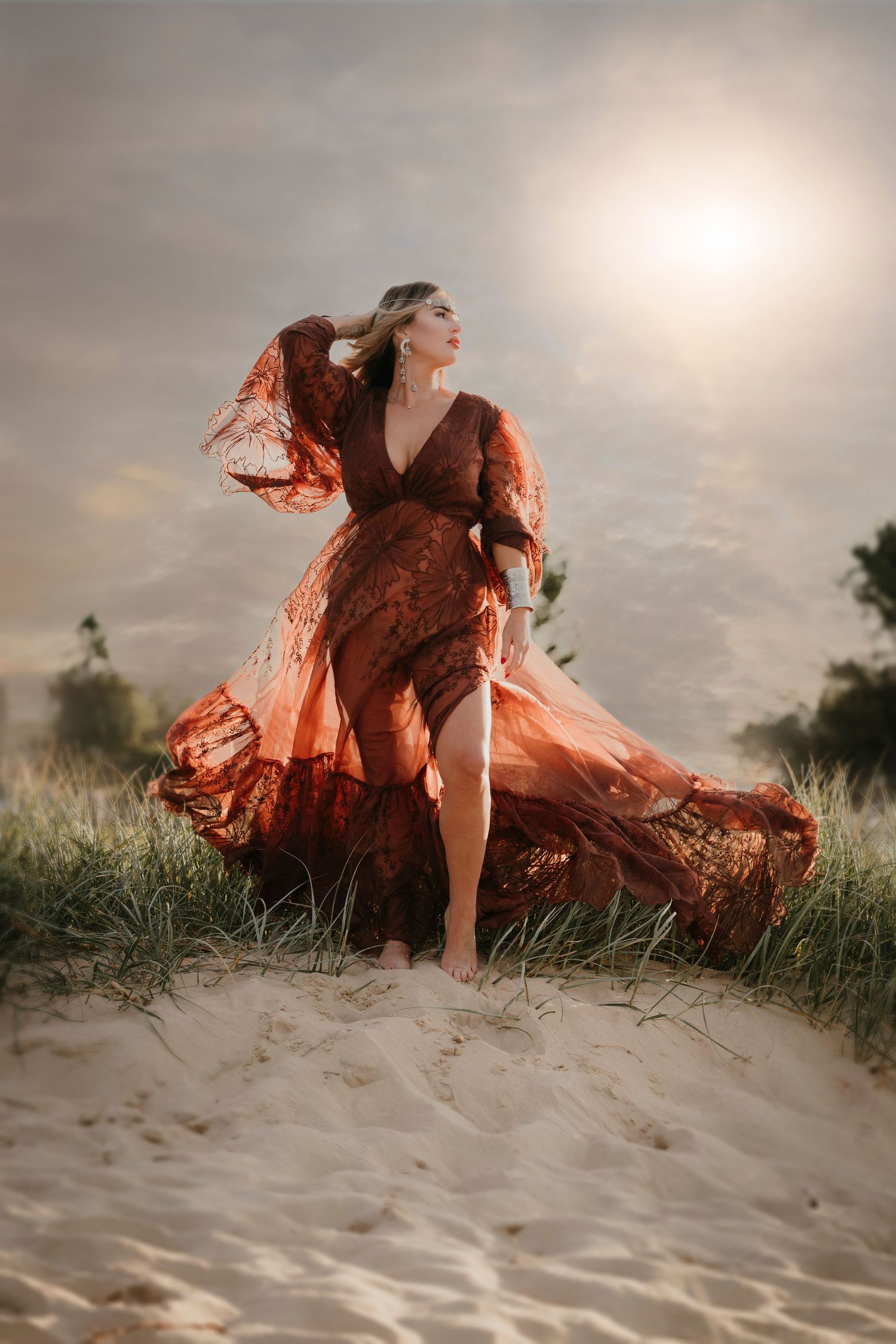 Flowing red dress catches wind as figure poses gracefully on sandy dunes at sunset.