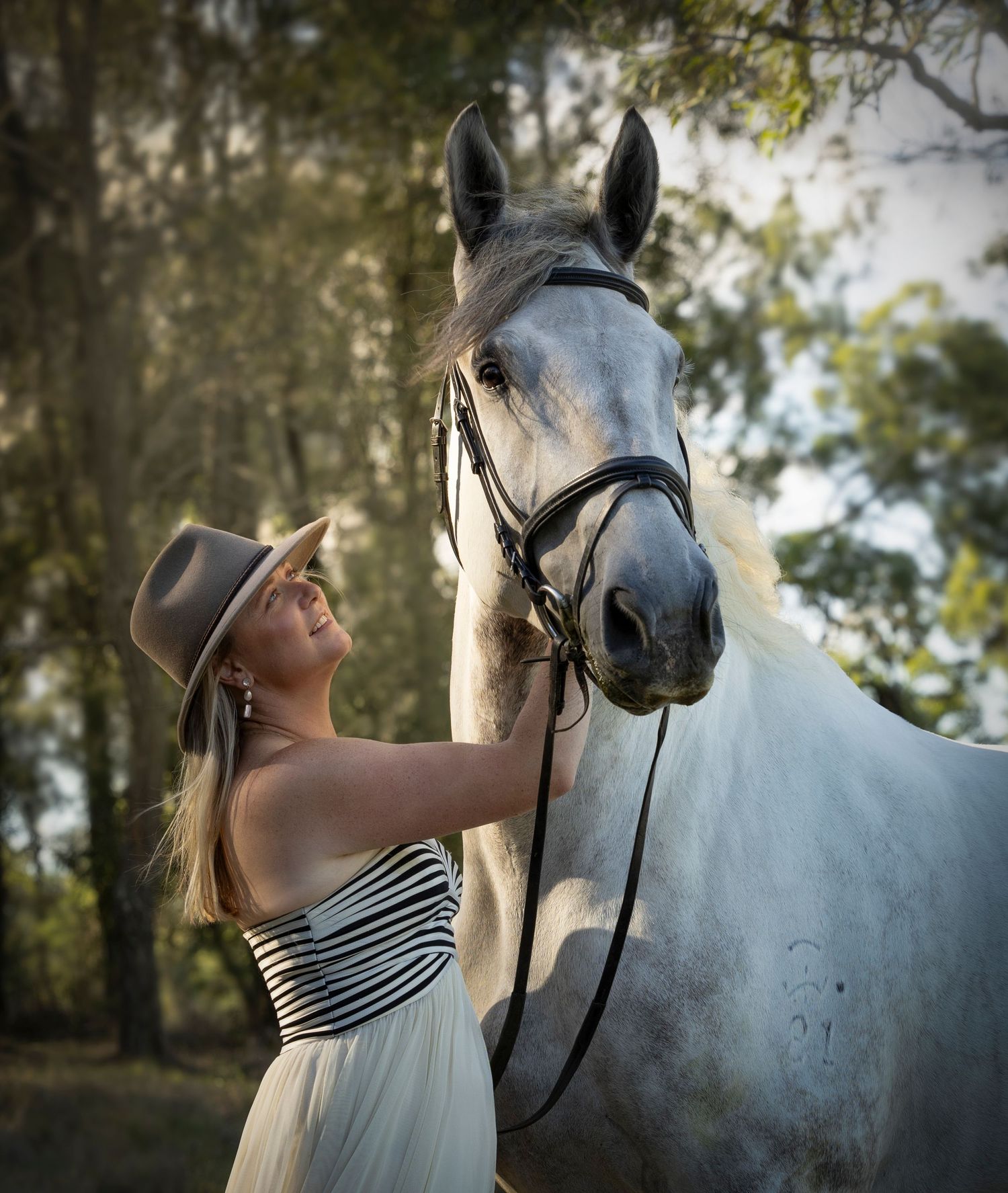 Elegant outdoor portrait with a white horse and striped sundress in natural lighting.