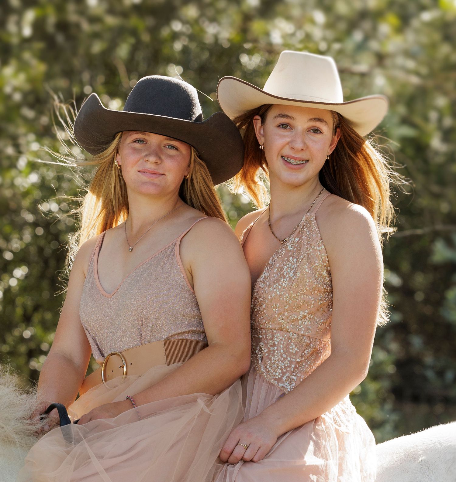 Two friends in cowboy hats and formal dresses pose together for an outdoor portrait.