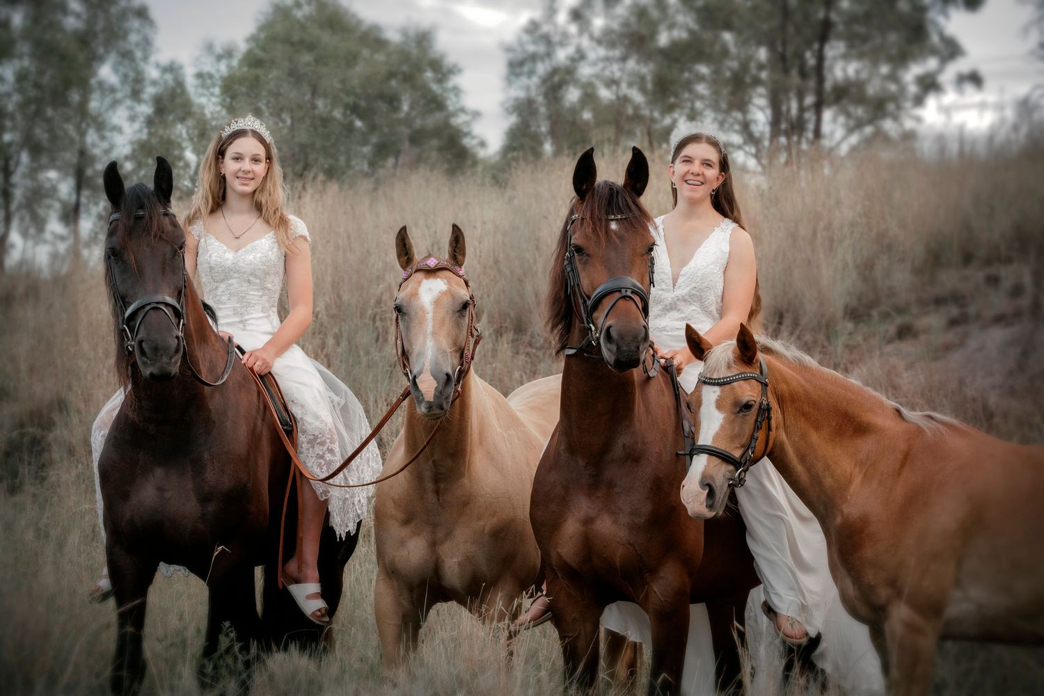 Two riders in white dresses sitting atop four majestic horses in a dreamy outdoor setting.