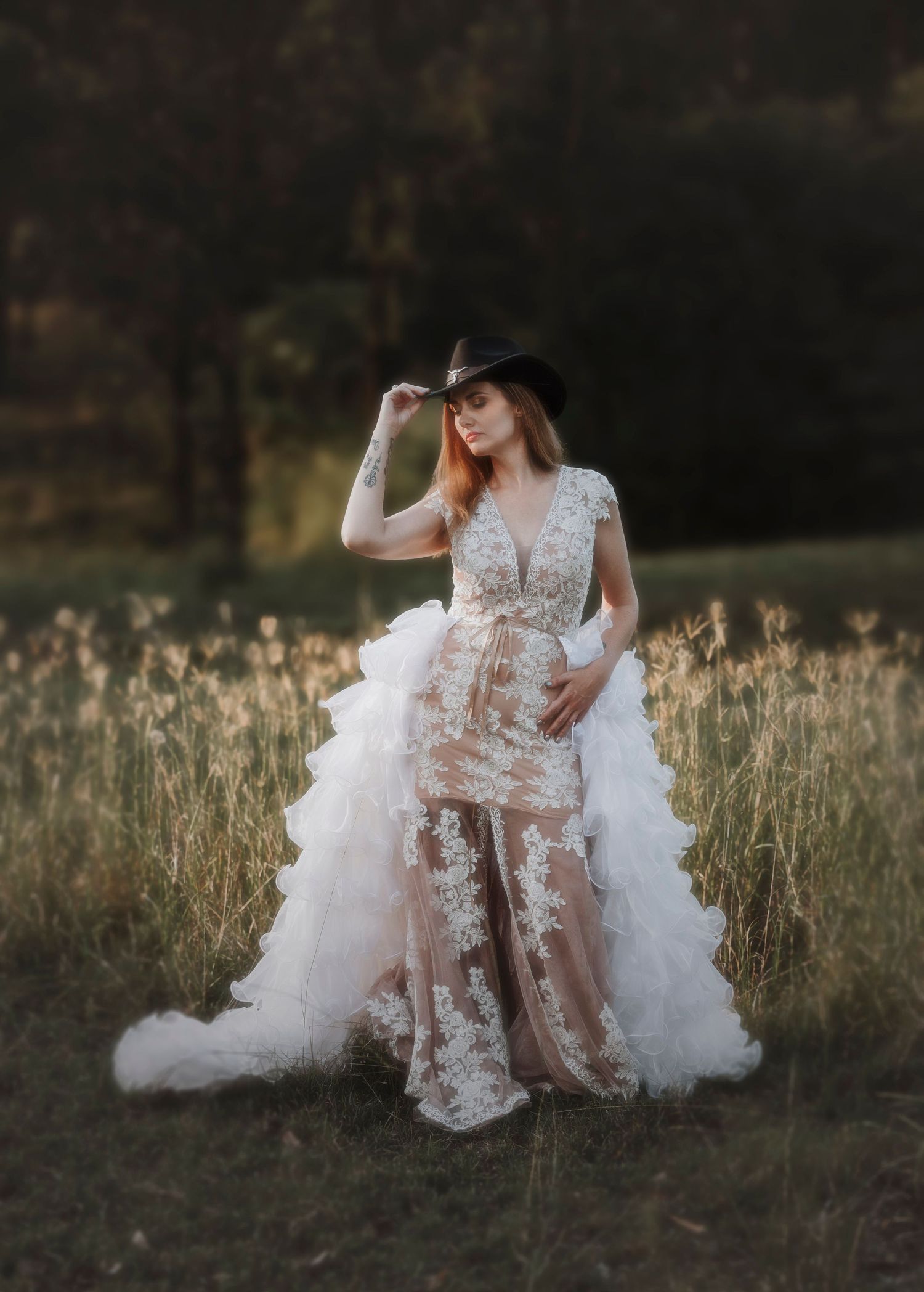 Ethereal lace wedding dress with sheer details and dramatic ruffled train photographed in a golden field at sunset.