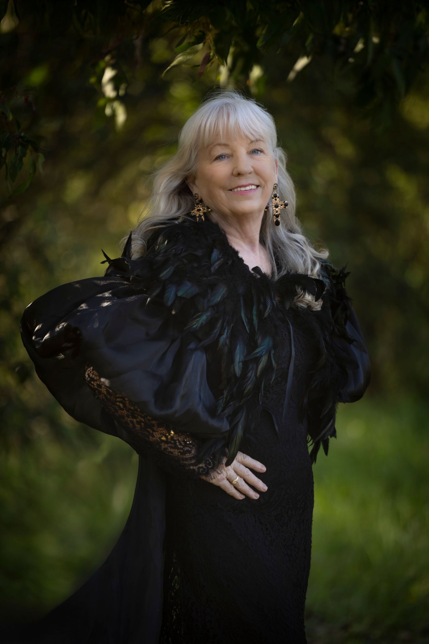 Elegant portrait in black feathered dress with lace details against natural garden backdrop.