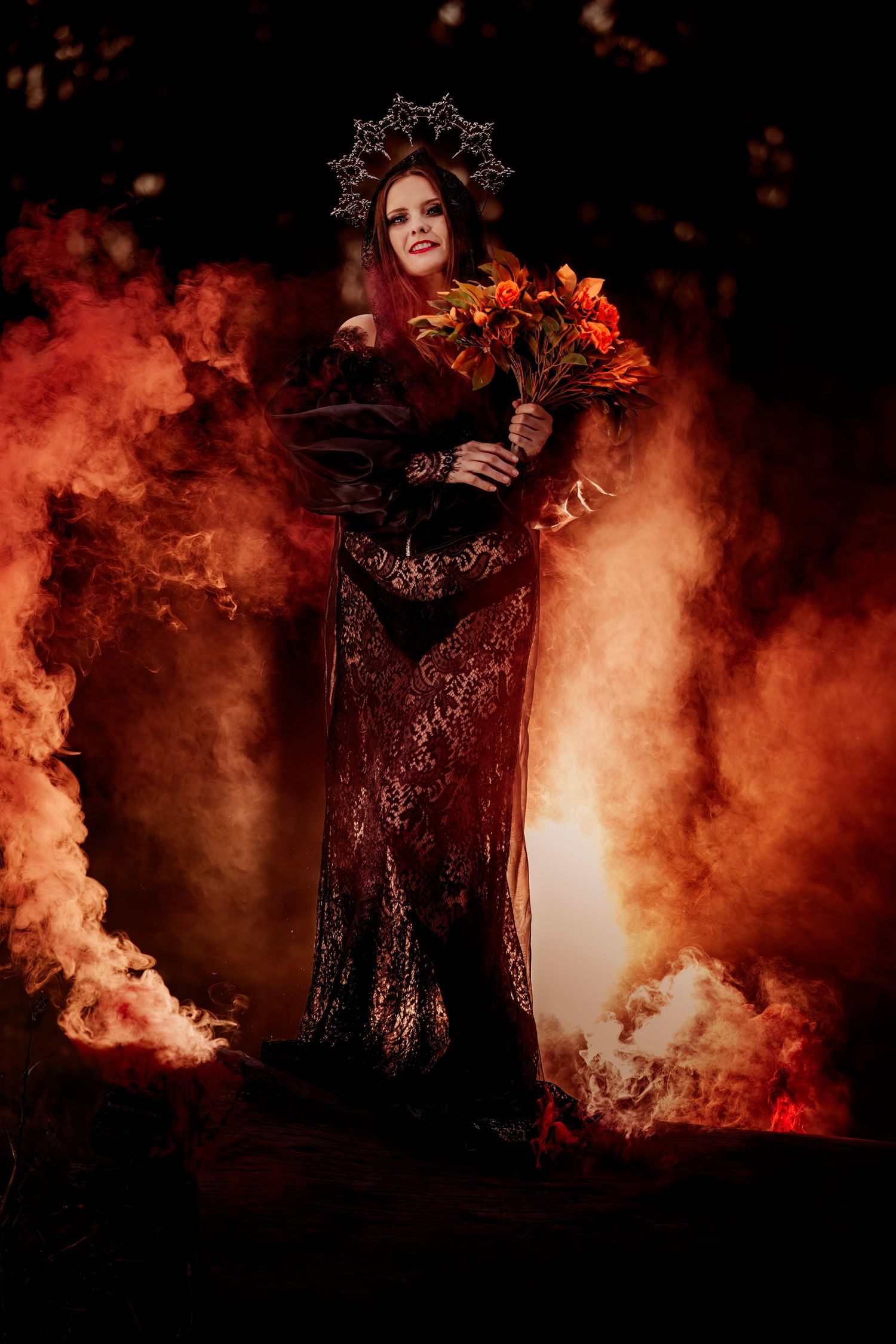 Dramatic portrait with orange smoke effects featuring dark lace dress and crown with autumn flowers.