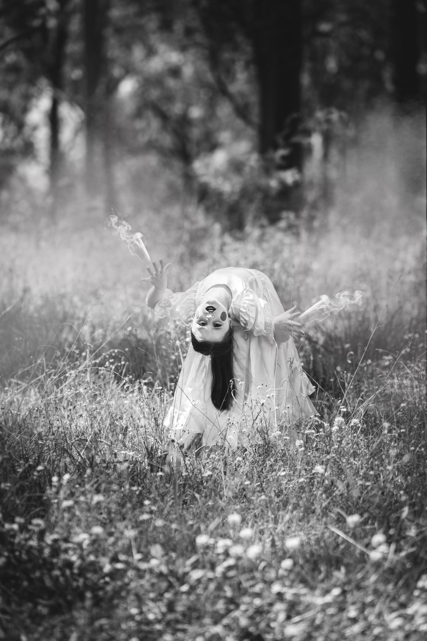 A figure in a white dress bends backwards gracefully in a misty meadow filled with wildflowers in black and white.