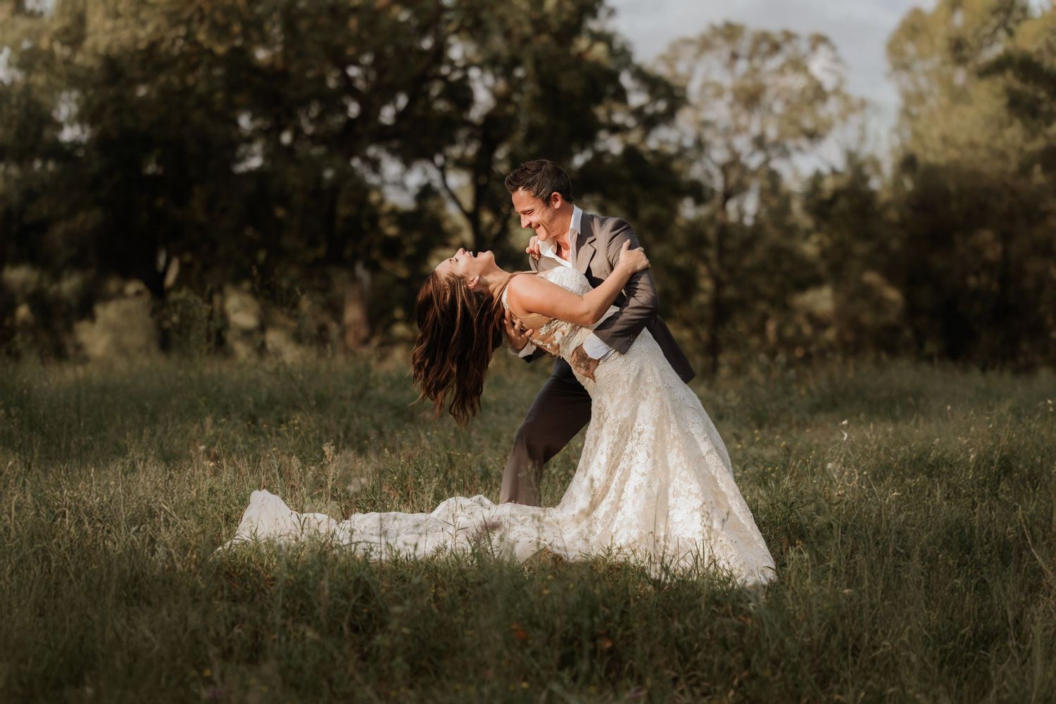 A romantic wedding couple embraces in a sunlit meadow during a dreamy outdoor photo session at sunset.
