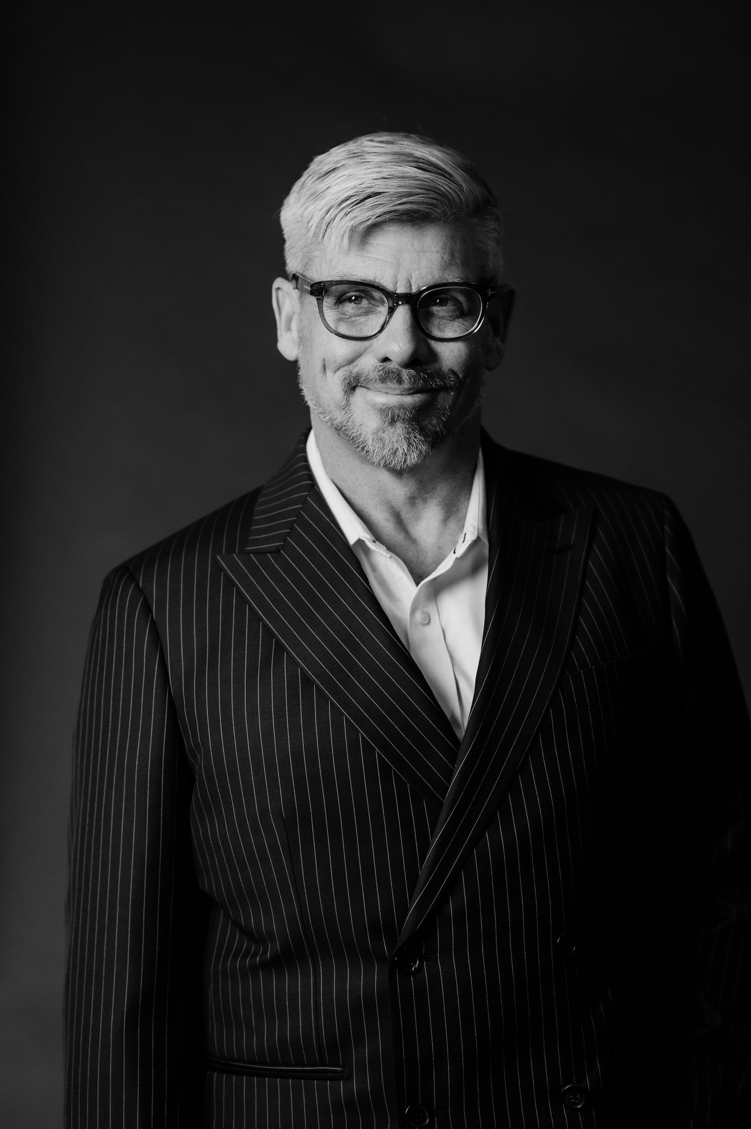 Professional black and white portrait series showing different angles of someone wearing a pinstriped suit and glasses.