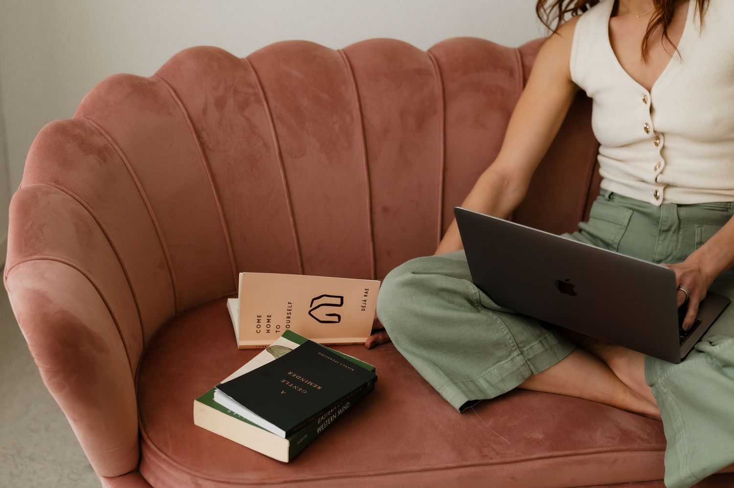 A person lounges on a pink velvet sofa with a book, wearing casual clothing in a cozy home setting.