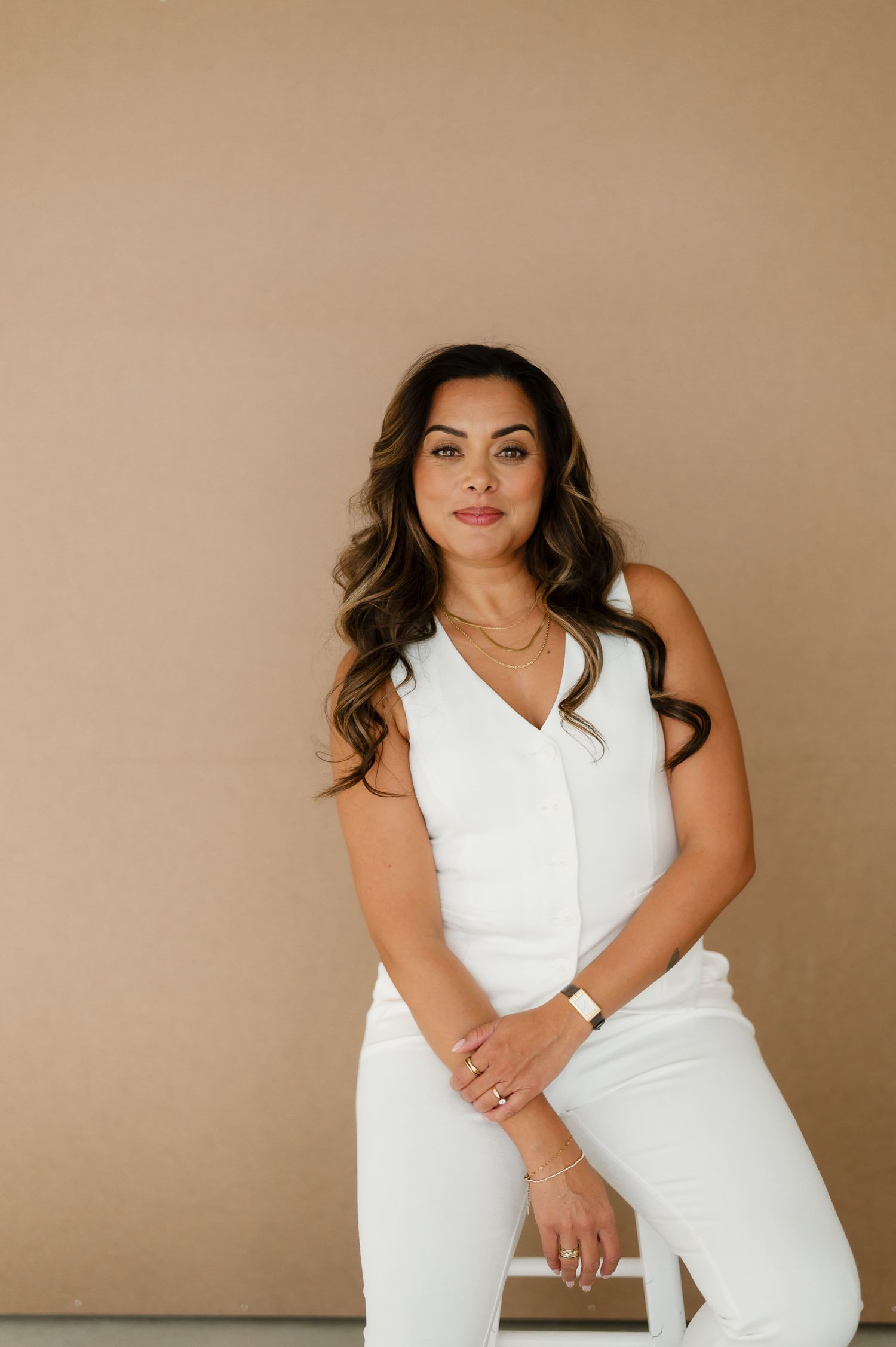 Professional studio portrait against beige background featuring a person in an elegant white outfit with wavy hair.