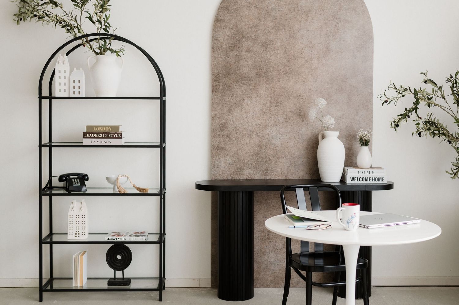 Modern minimalist dining room with black shelving units, white walls, and natural greenery accents.