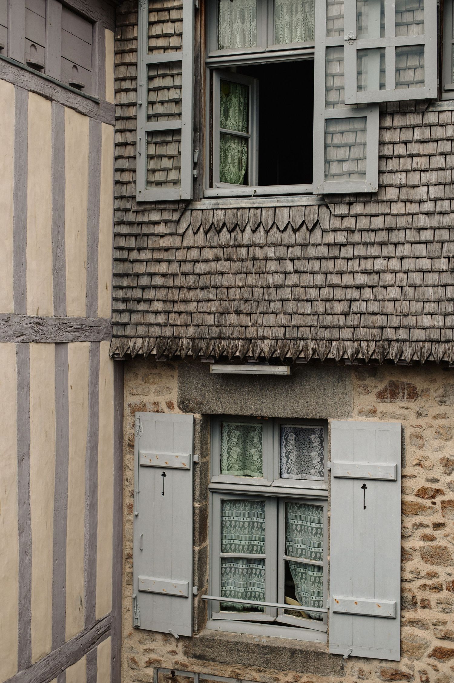 Historic half-timbered building with gray wooden shuttered windows and decorative shingle facade in a French medieval town.