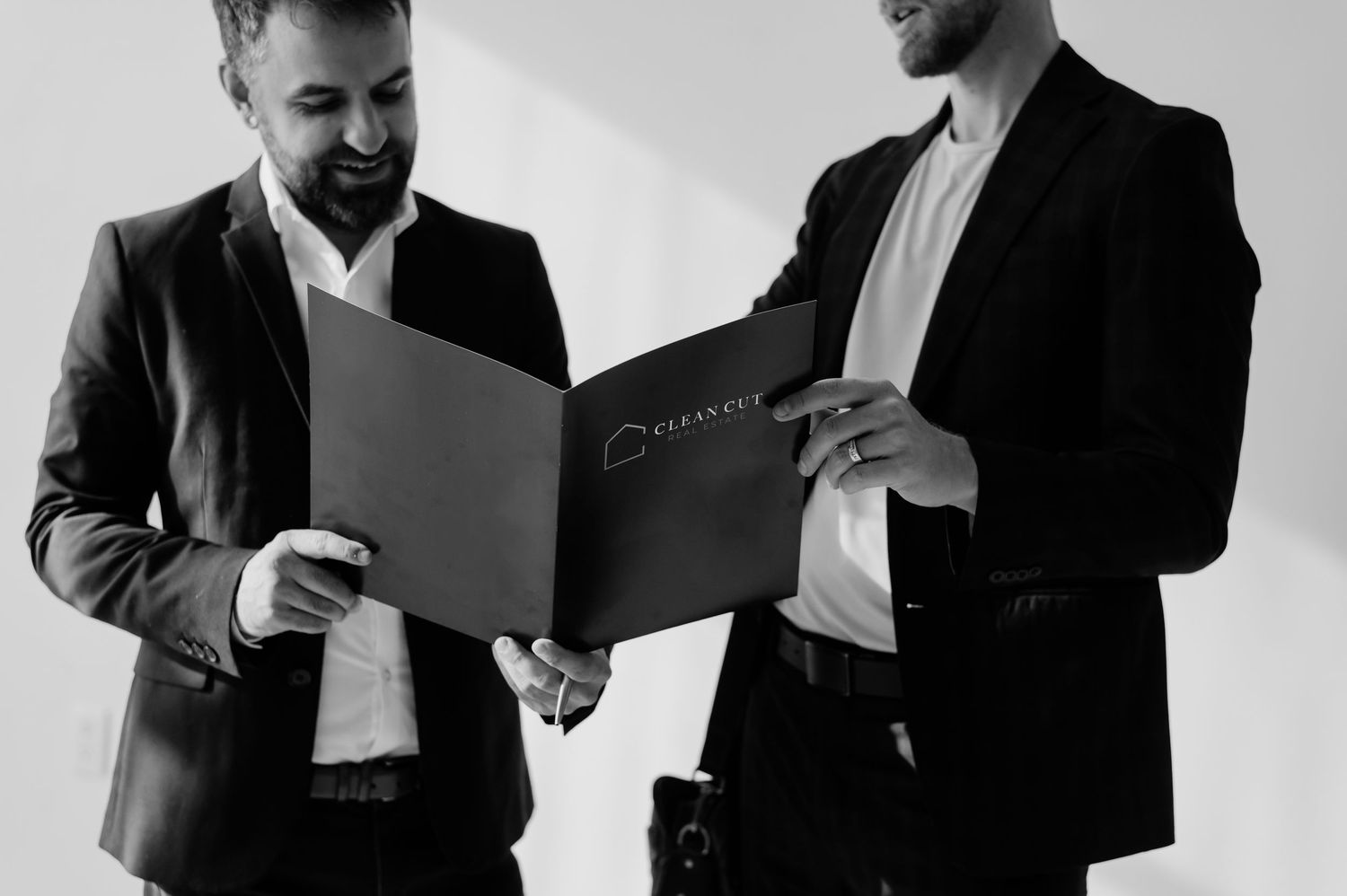 Two businessmen in suits reviewing documents in a black and white professional meeting setting.