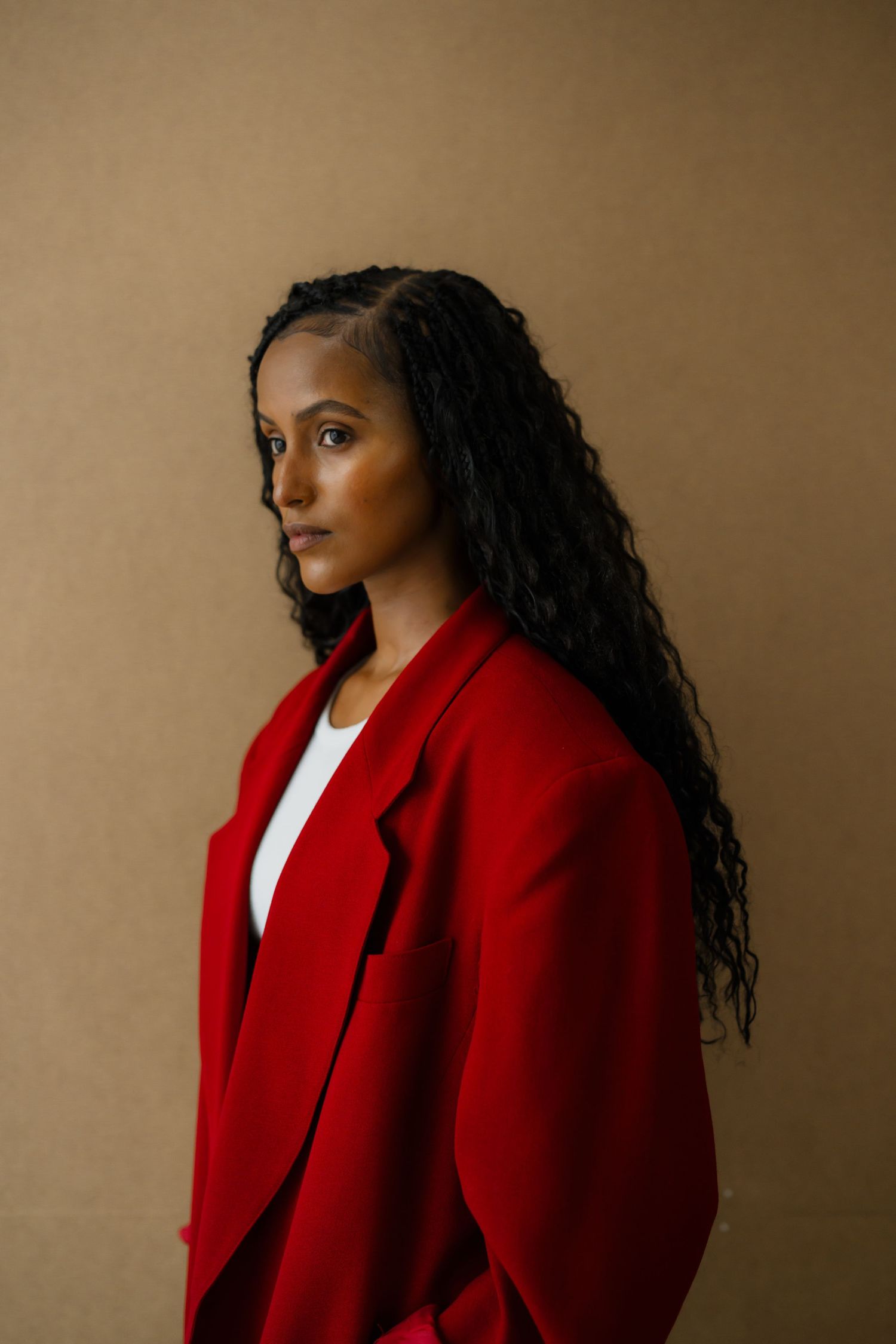 Woman in bold red blazer with long curly hair posing against warm beige background.