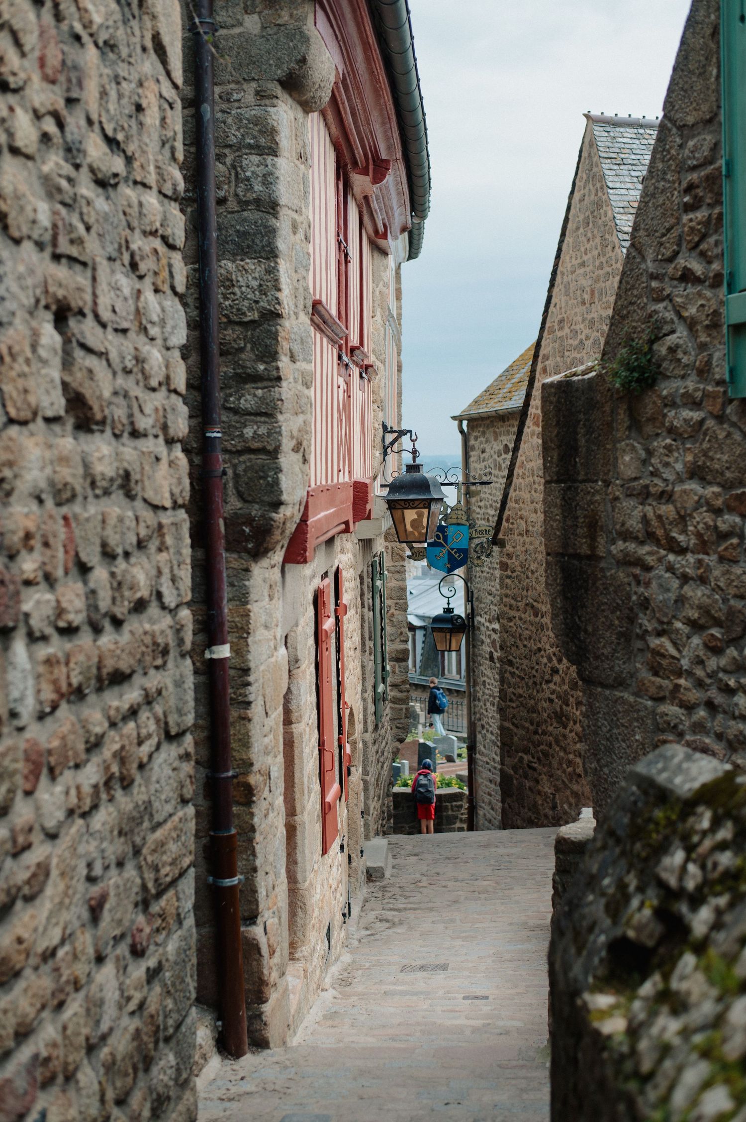 A narrow cobblestone alley lined with historic stone buildings and a vintage lantern in Mont Saint-Michel.