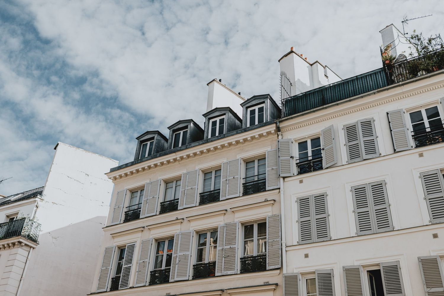 Classic Parisian Haussmann-style white buildings with mansard roofs, dormer windows, and wrought-iron balconies under a cloudy sky.