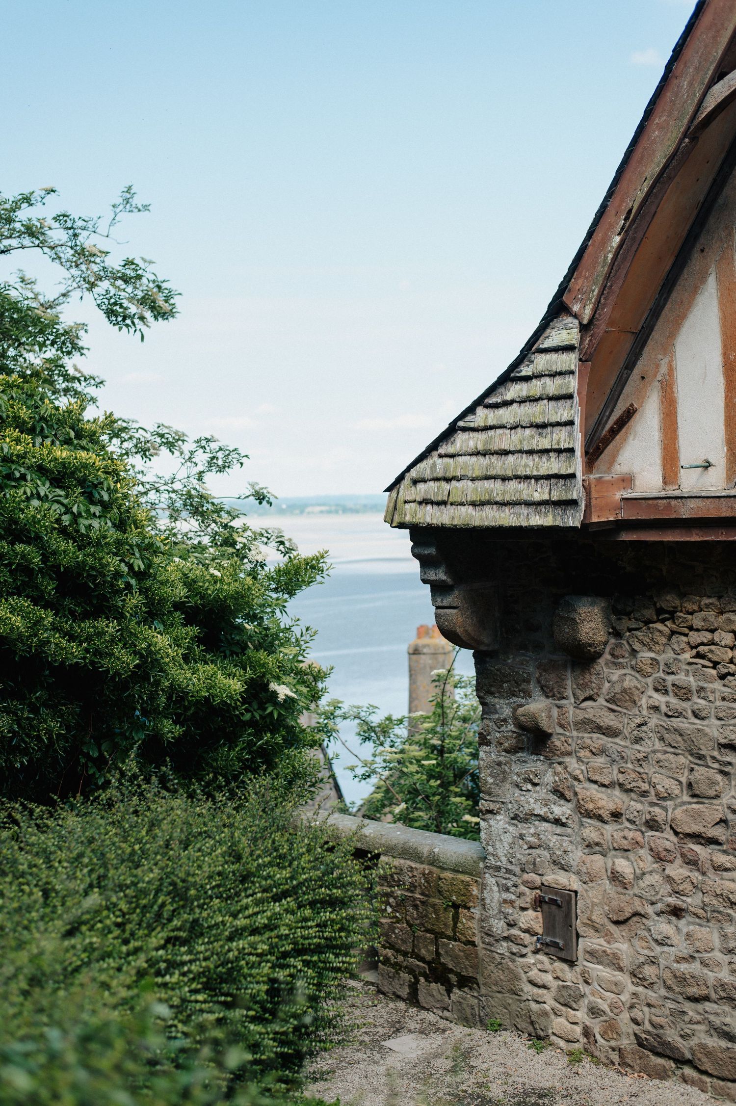 Stone building with curved wooden roof eave overlooking a serene lake, surrounded by lush green trees under a clear sky.