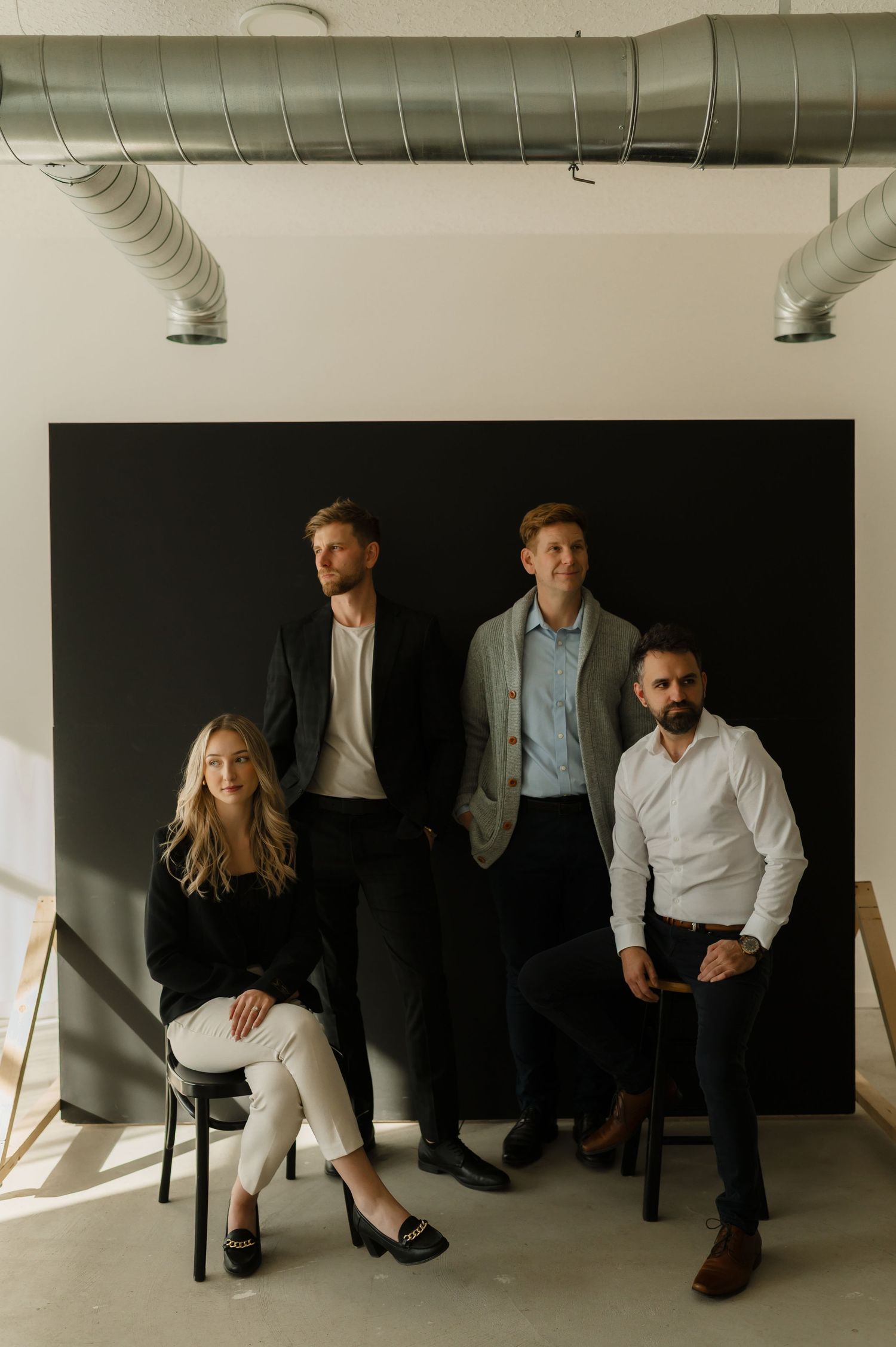Four professionals pose for a modern team photo against a black backdrop in a minimalist studio space.