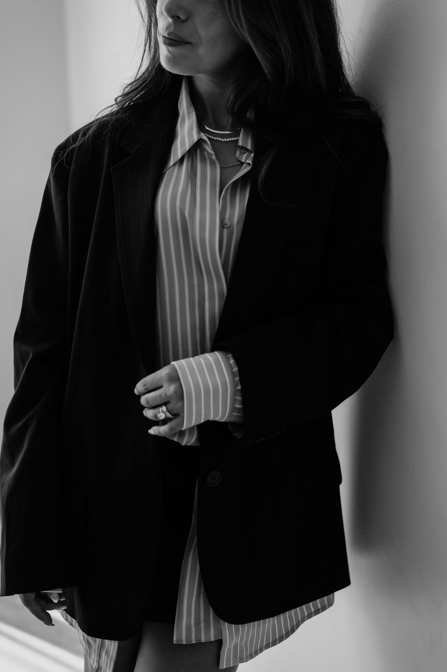 Black and white fashion photo showing a person wearing a striped button-down shirt layered under an oversized black blazer.