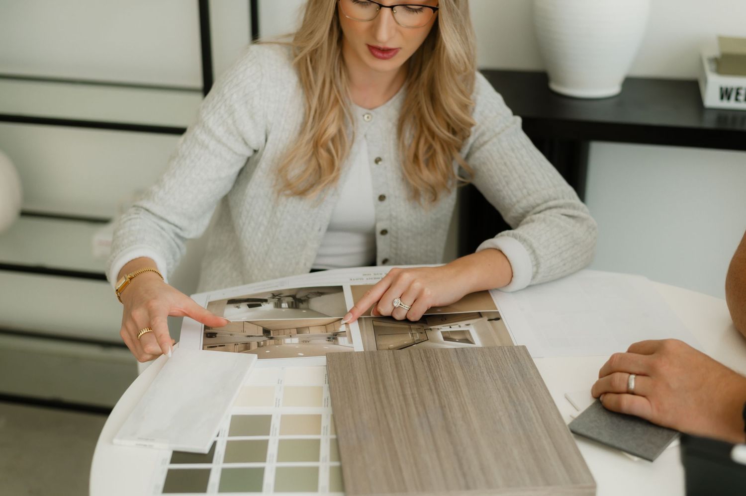Interior designer presenting material samples and color swatches to a client at a modern white desk.