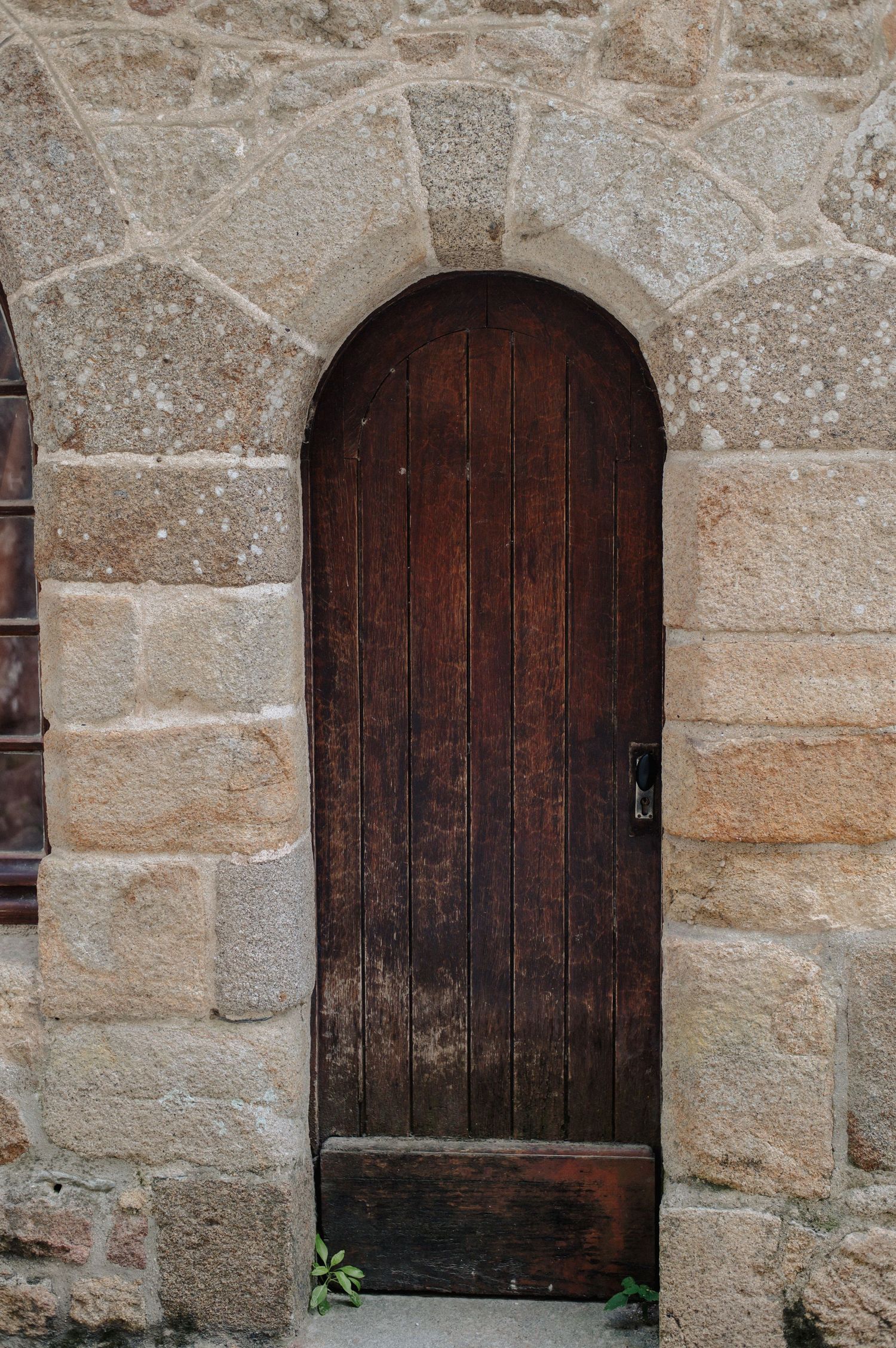 Ancient arched wooden door set in rustic stone wall with keyhole lock, medieval architecture detail.