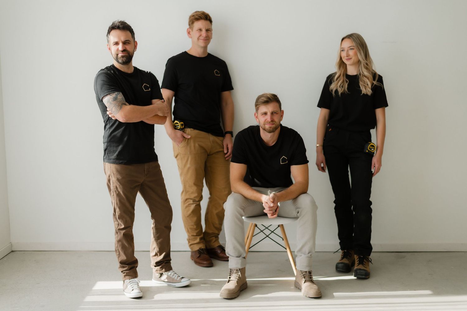 Four team members in matching black branded shirts pose together in a bright white studio setting.
