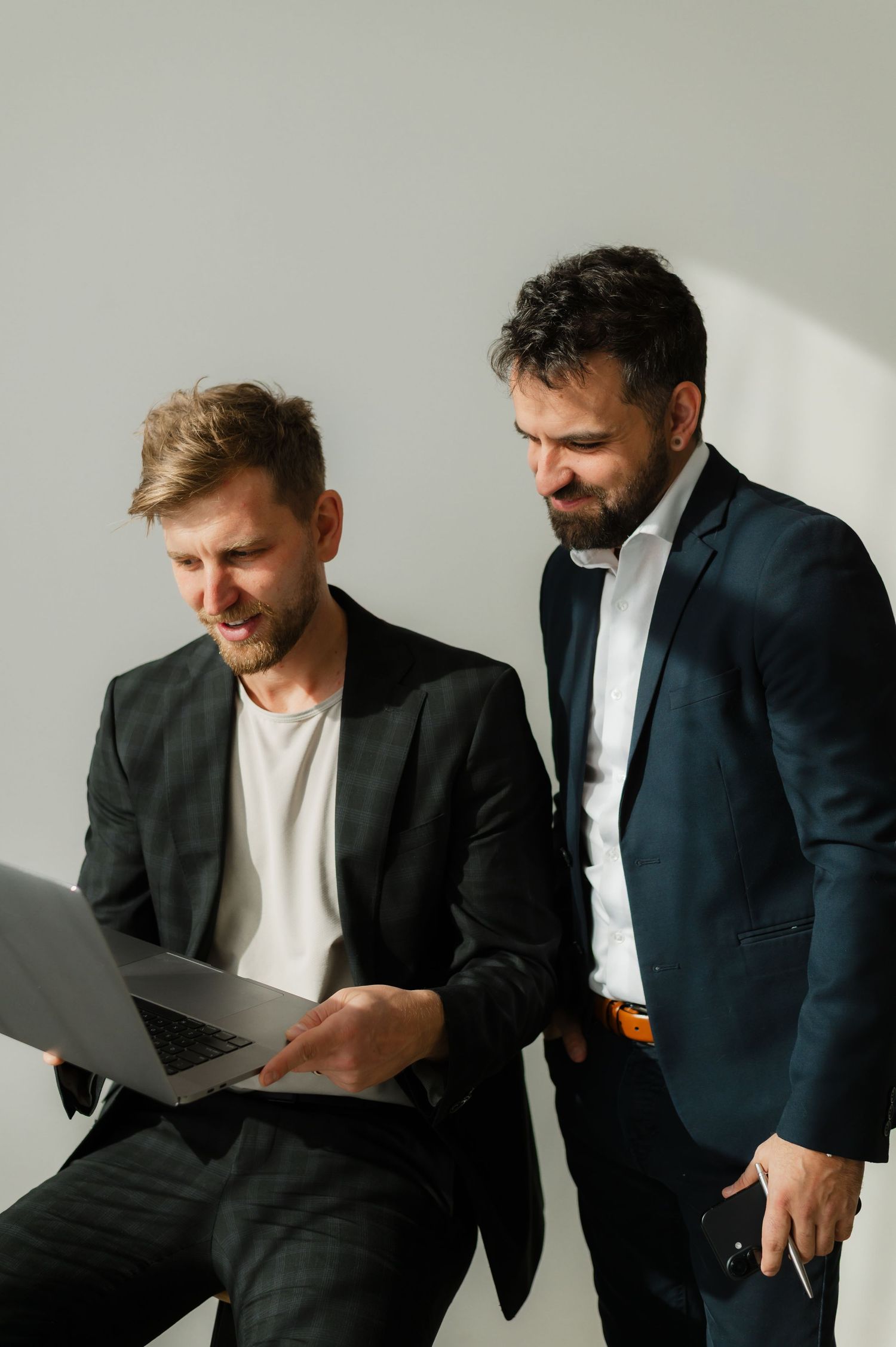 Two businessmen in suits reviewing work on a laptop together in a bright office setting.