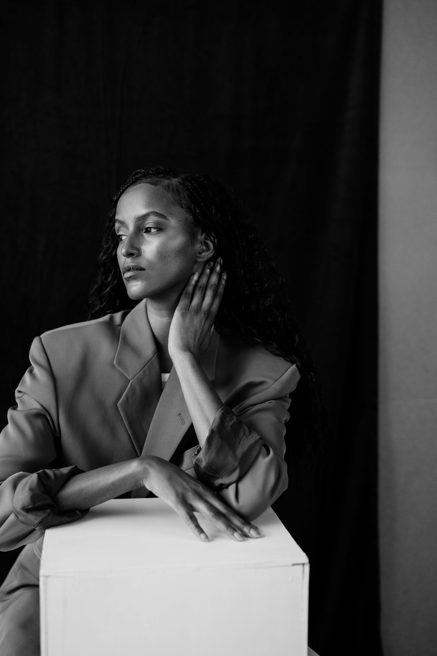 Black and white portrait of woman in blazer resting hand on face beside white cube.