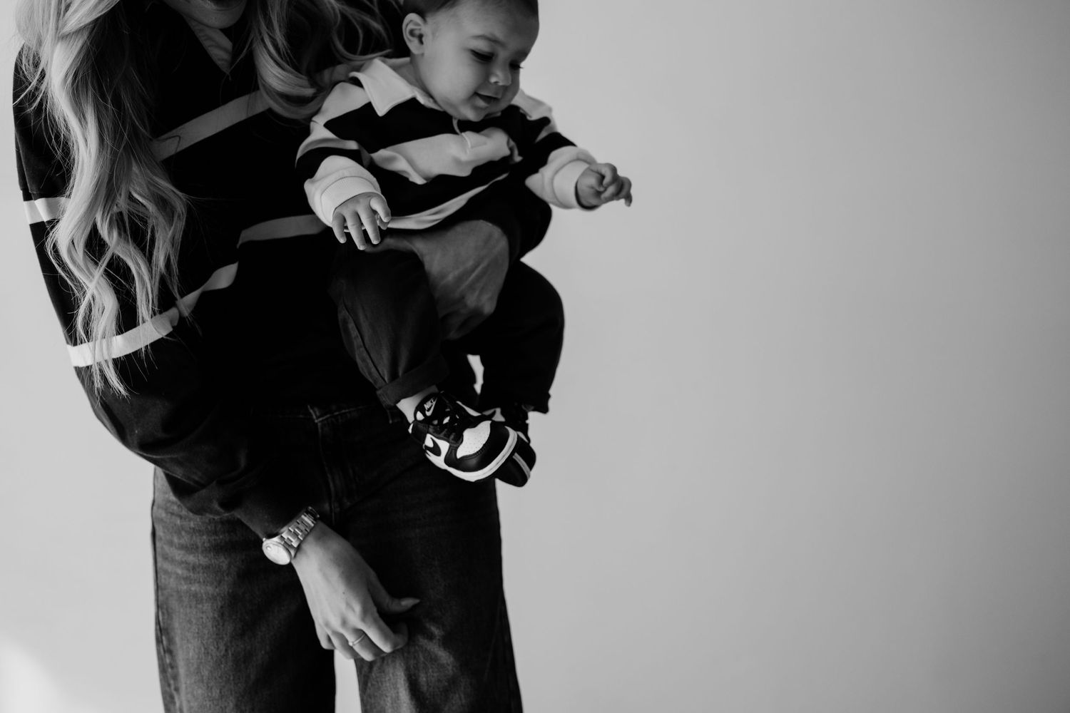 Black and white photo of a woman holding a young toddler boy dressed in a striped shirt and sneakers.