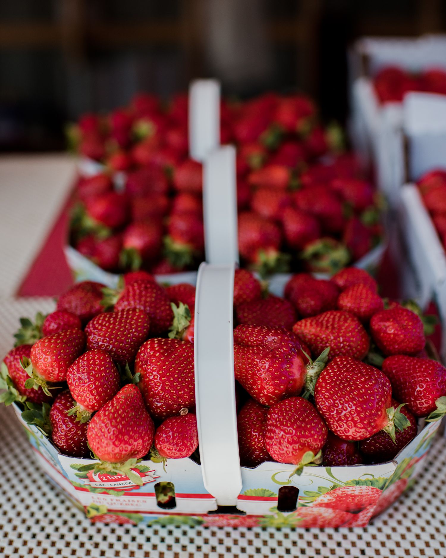 Fresh red strawberries piled in decorative cardboard baskets at a farmers market display.