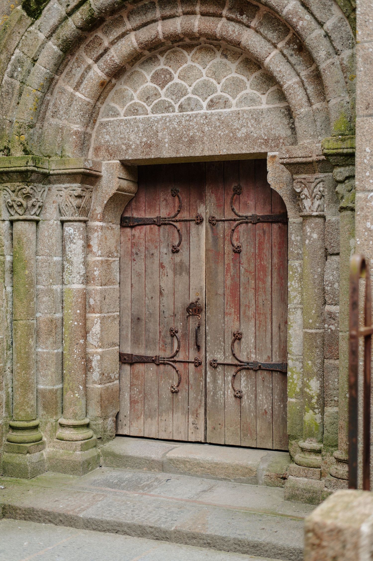 Ancient wooden double doors with ornate iron hinges beneath a carved Romanesque stone arch with columns.