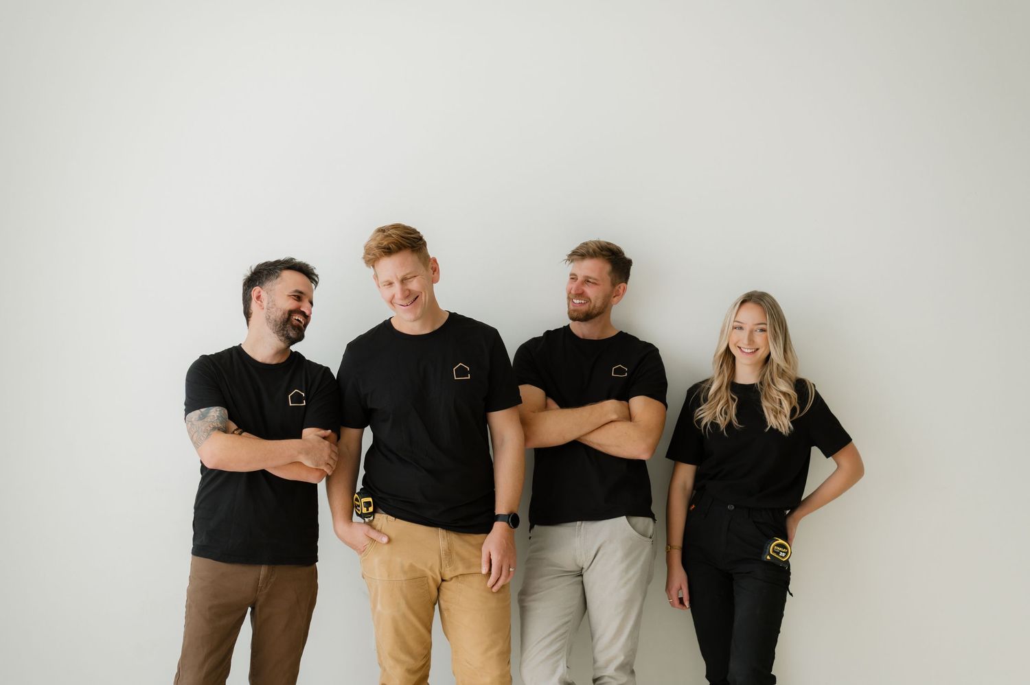 Four colleagues in matching black t-shirts smiling and laughing together against a white background.