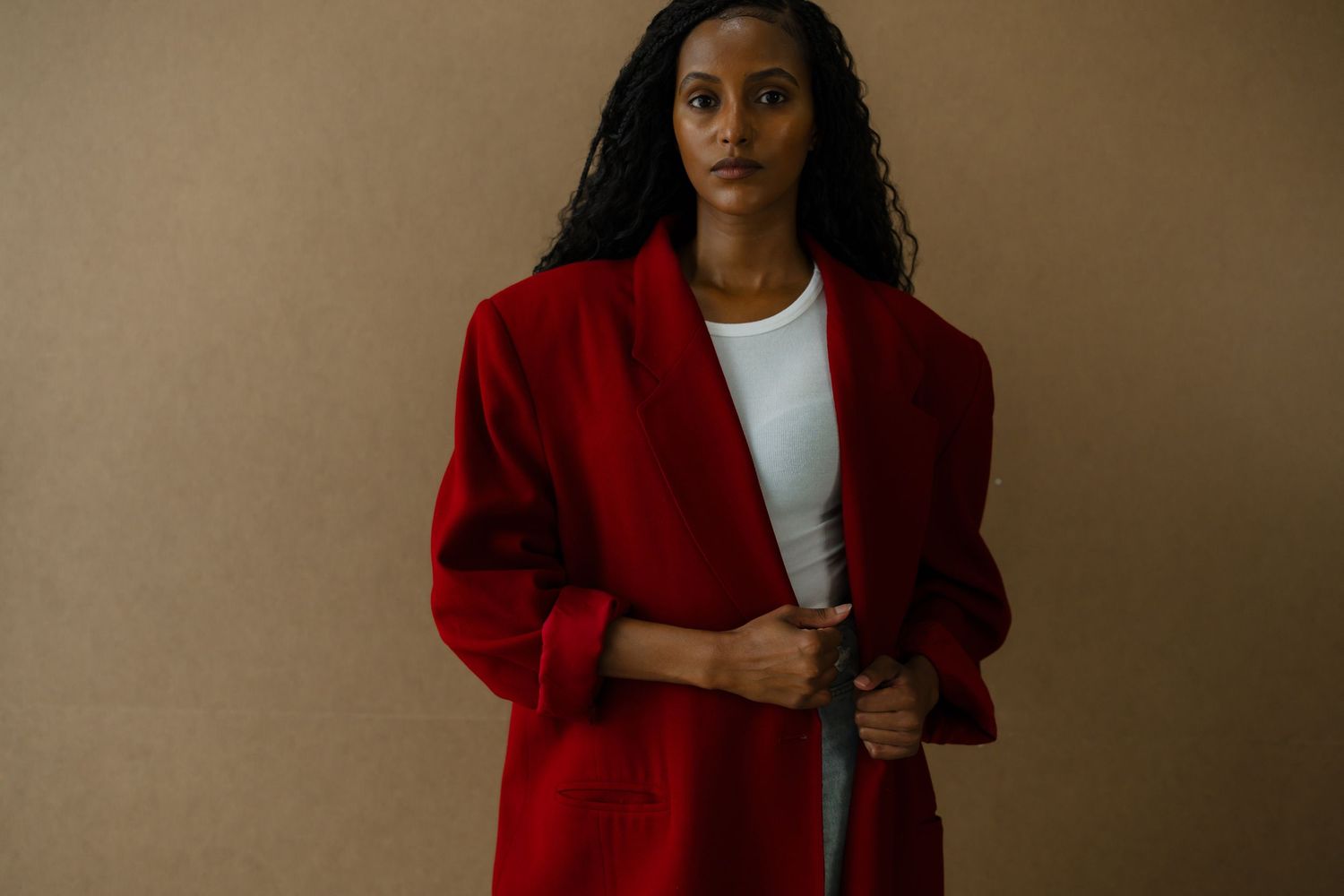 Woman in oversized red blazer and white top posing against beige background.
