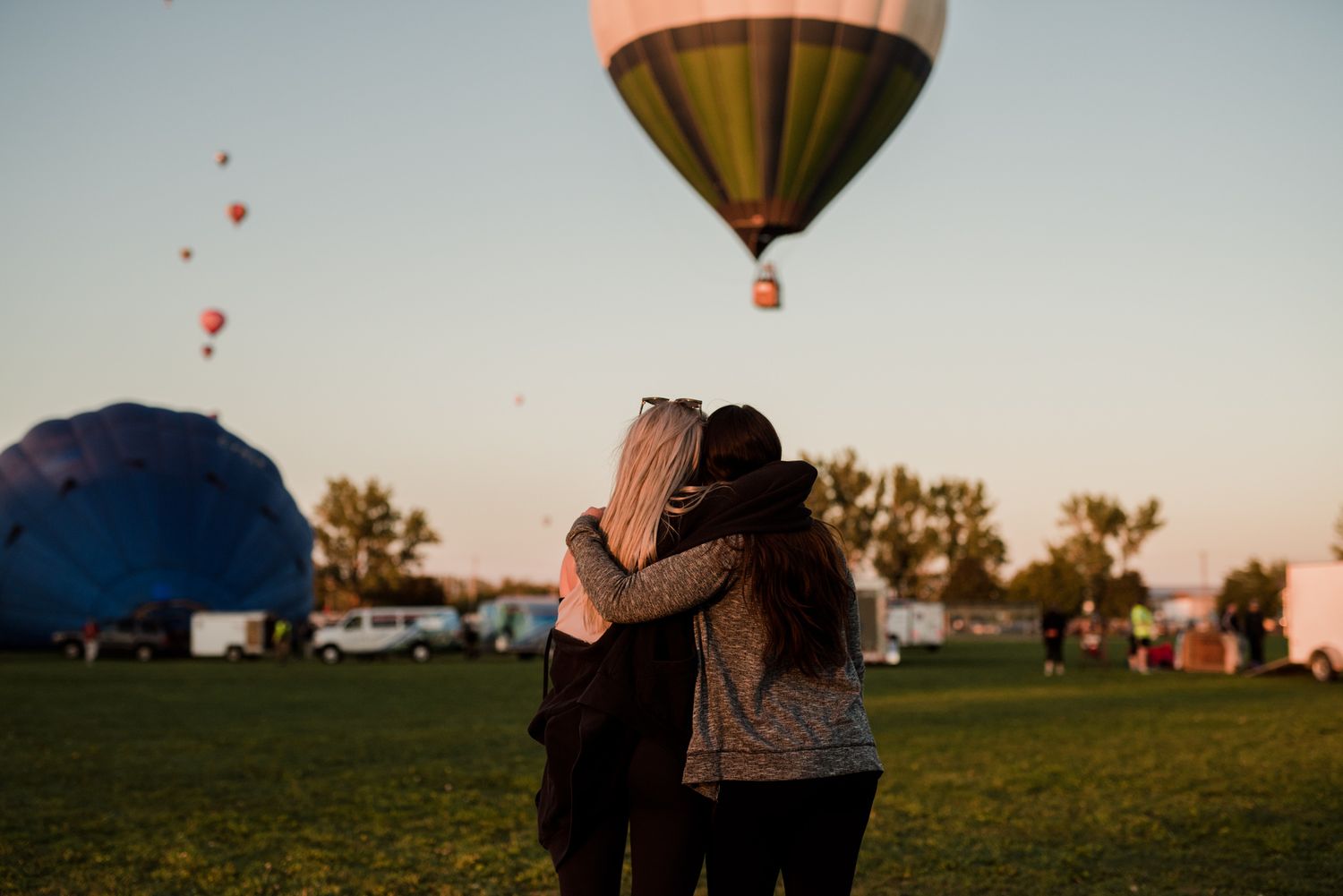 Two people embracing while watching colorful hot air balloons rise at sunset.
