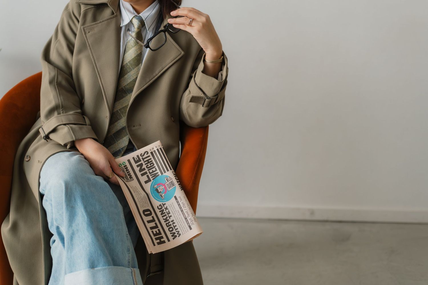 Person wearing a beige jacket holds a vintage Polaroid camera while sitting in a brown leather chair.