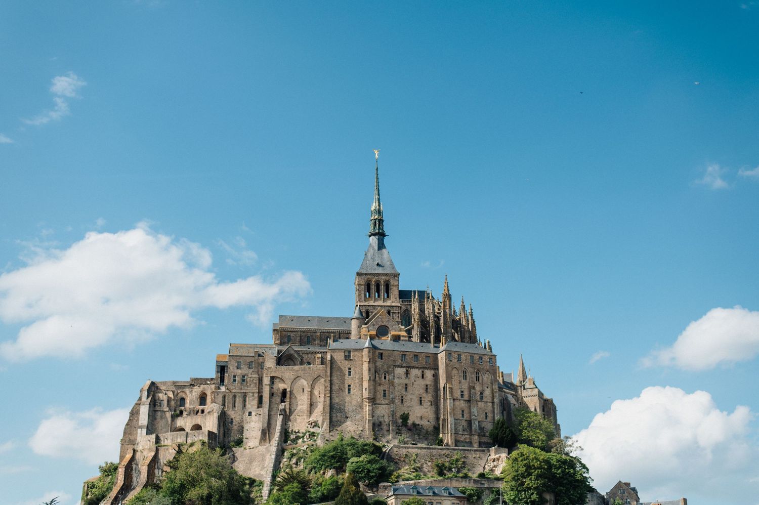 Mont Saint-Michel abbey rising dramatically on a rocky island under a blue sky in Normandy, France.