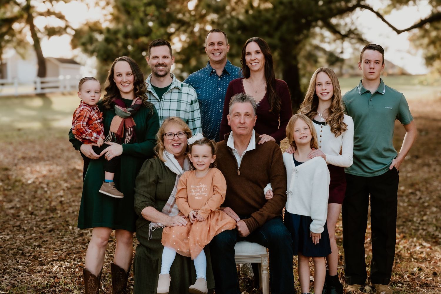 A group of people wearing coordinated green and white outfits pose together outdoors during a fall photo session.