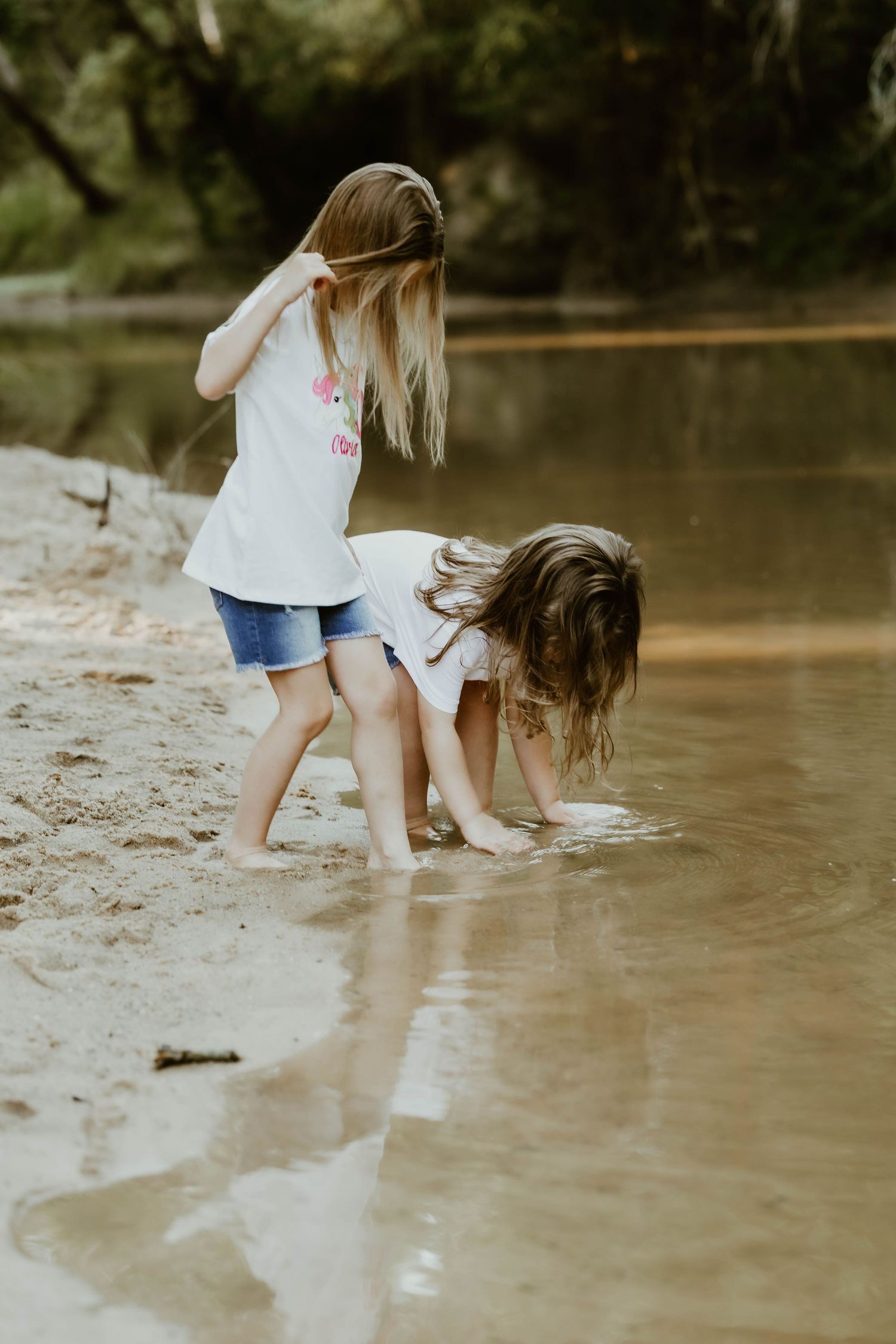 Two children splashing and playing in shallow river water on sunny day.