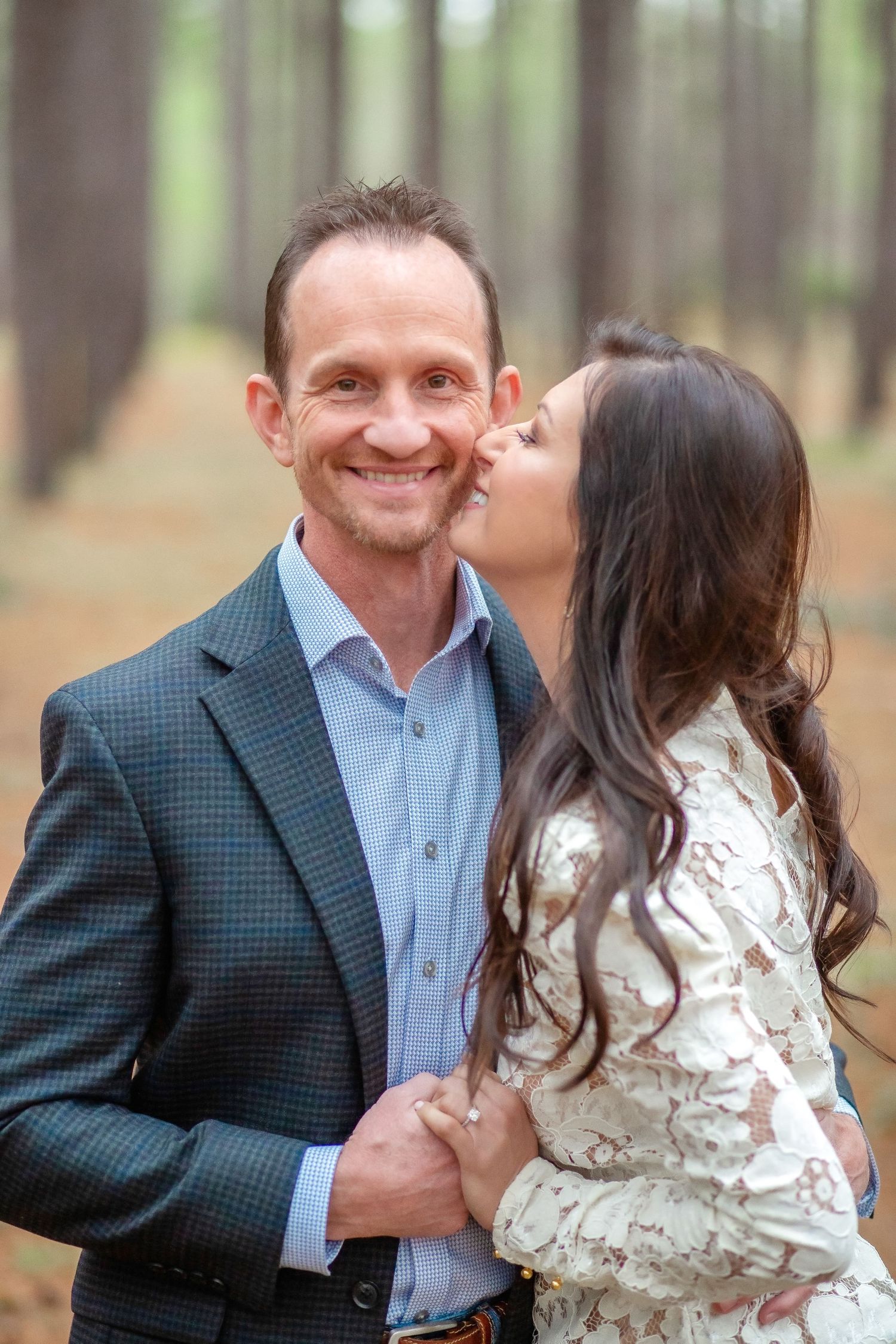 A romantic couple embraces and laughs together during an outdoor photo session in a wooded setting.