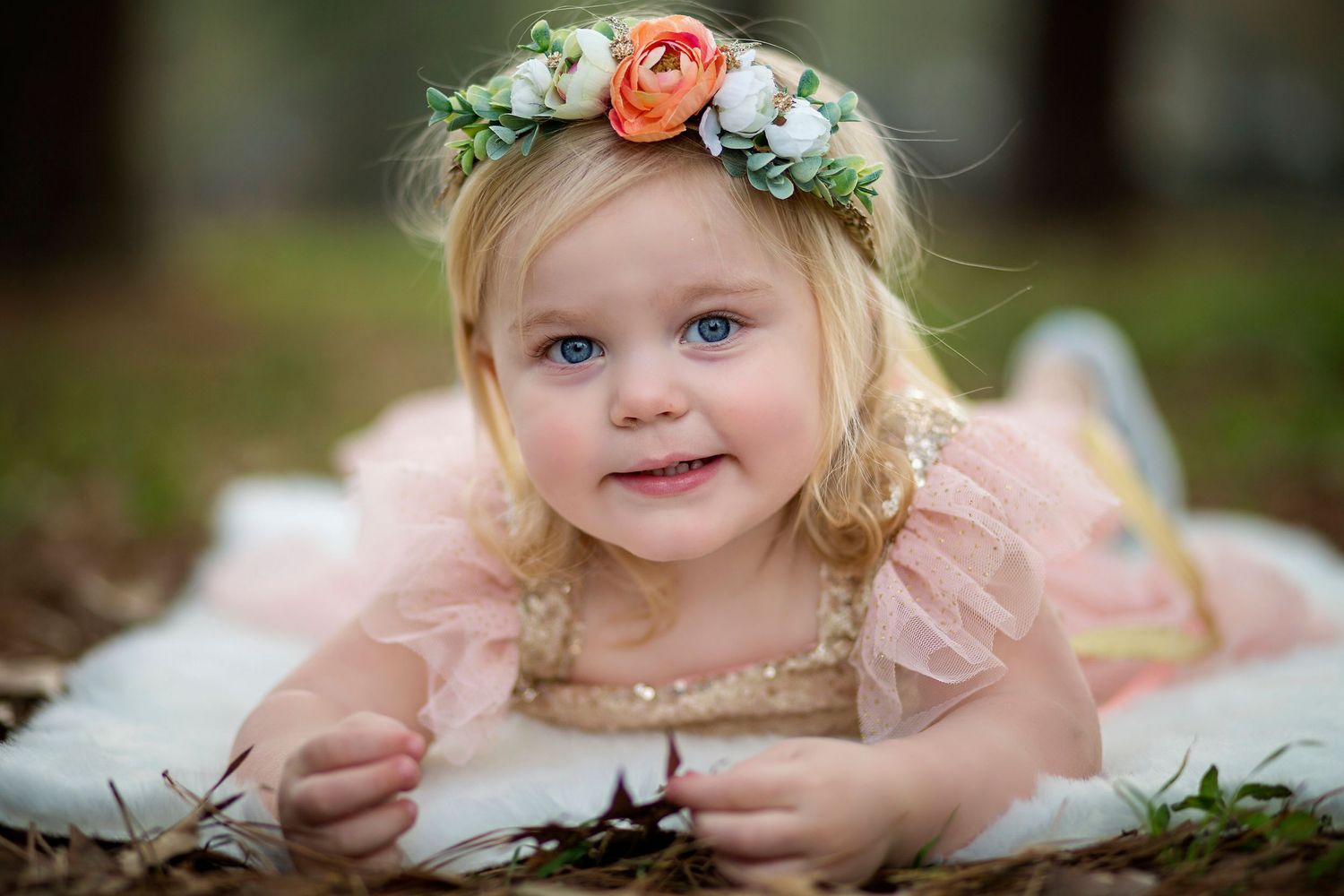 A young child wearing a floral crown and peach dress poses for outdoor portraits.