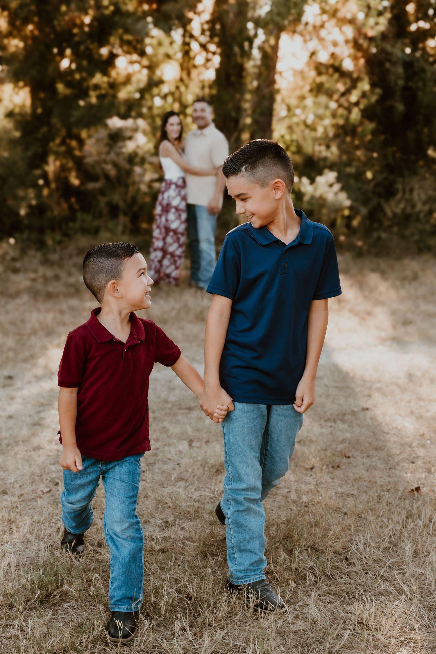 Two people in jeans share a playful moment together while walking on dry grass at sunset.