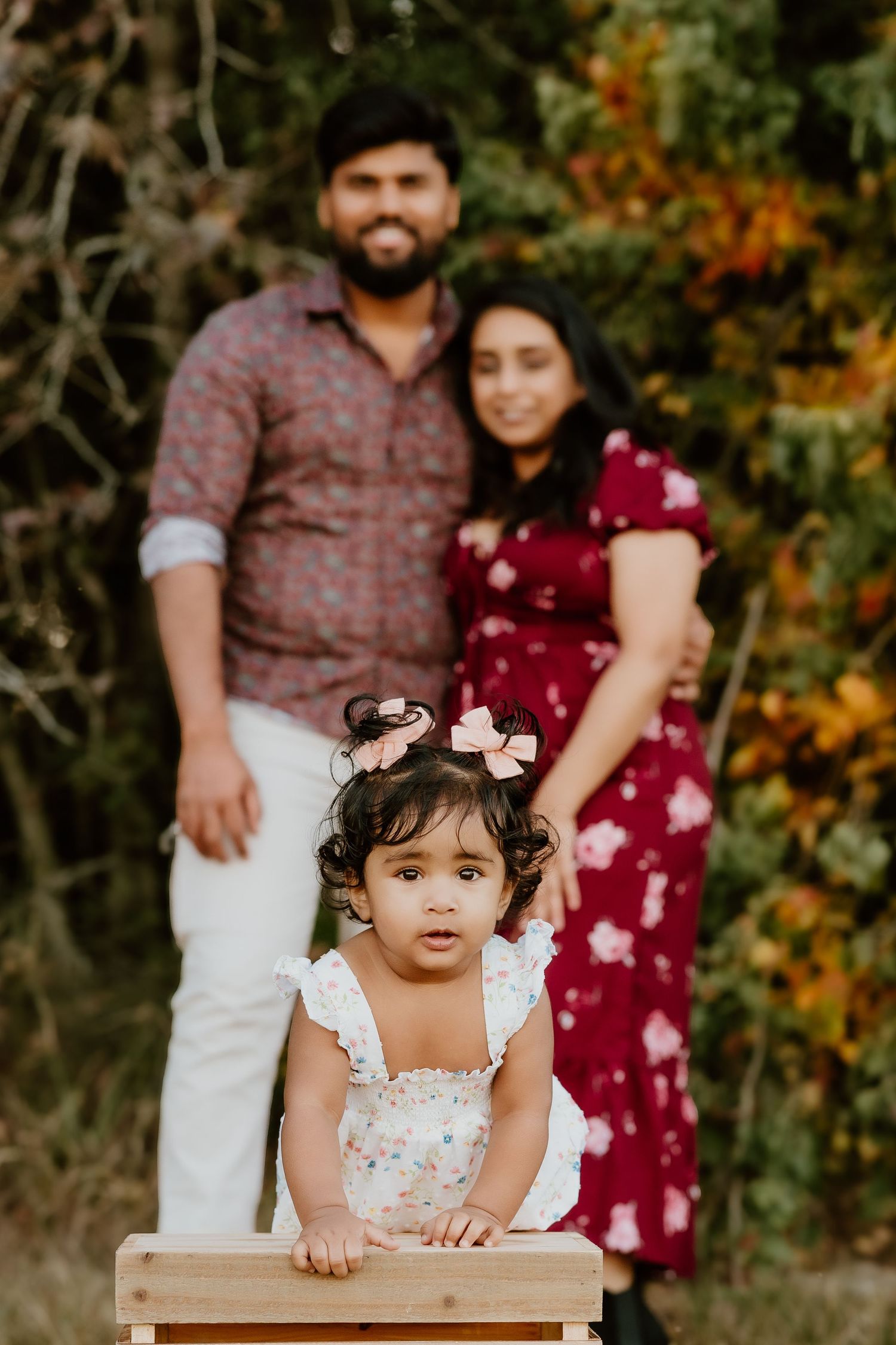 A family poses together in an outdoor autumn setting with warm fall colors and natural foliage in the background.