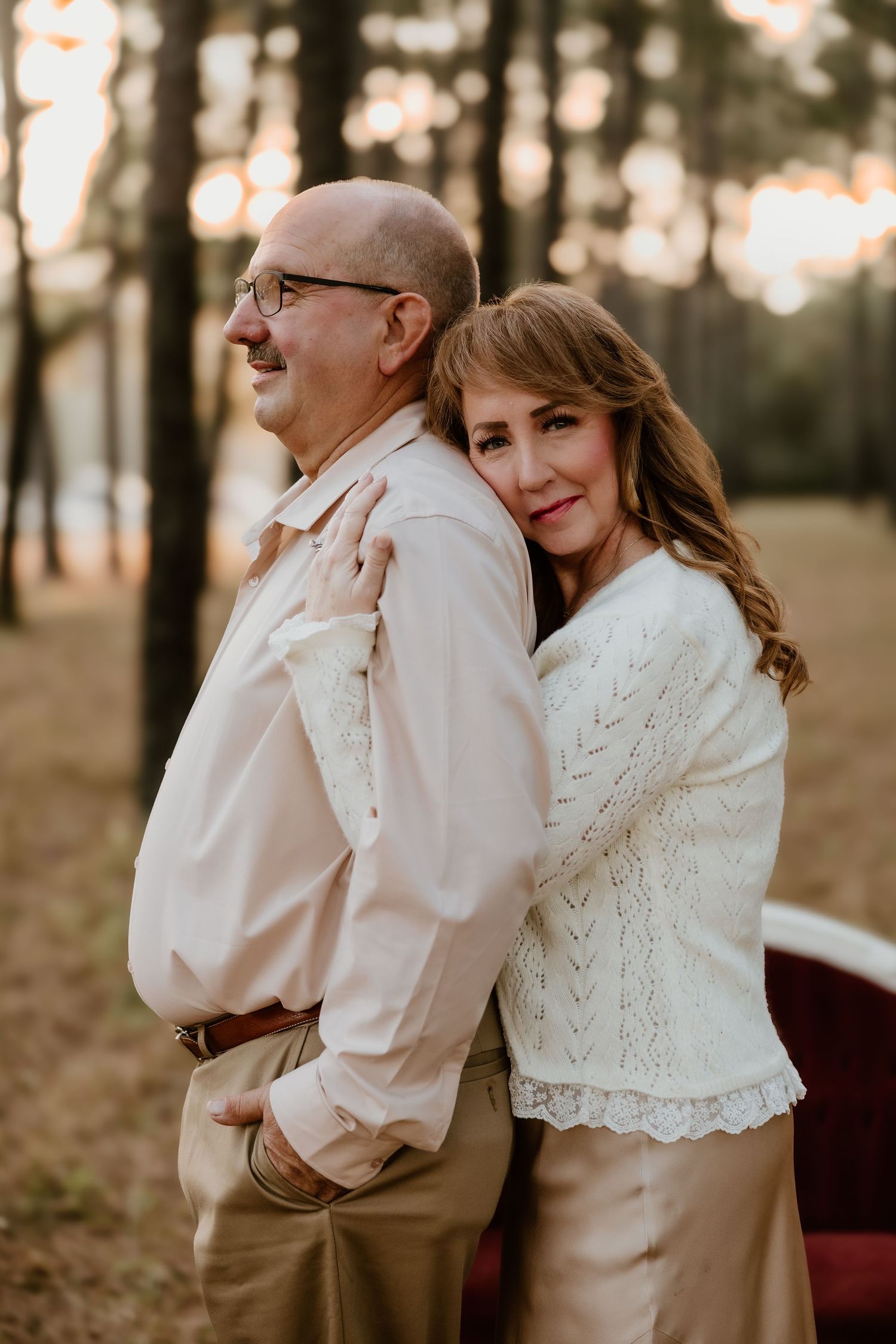 A couple shares an intimate moment dancing together in a wooded outdoor setting at sunset.