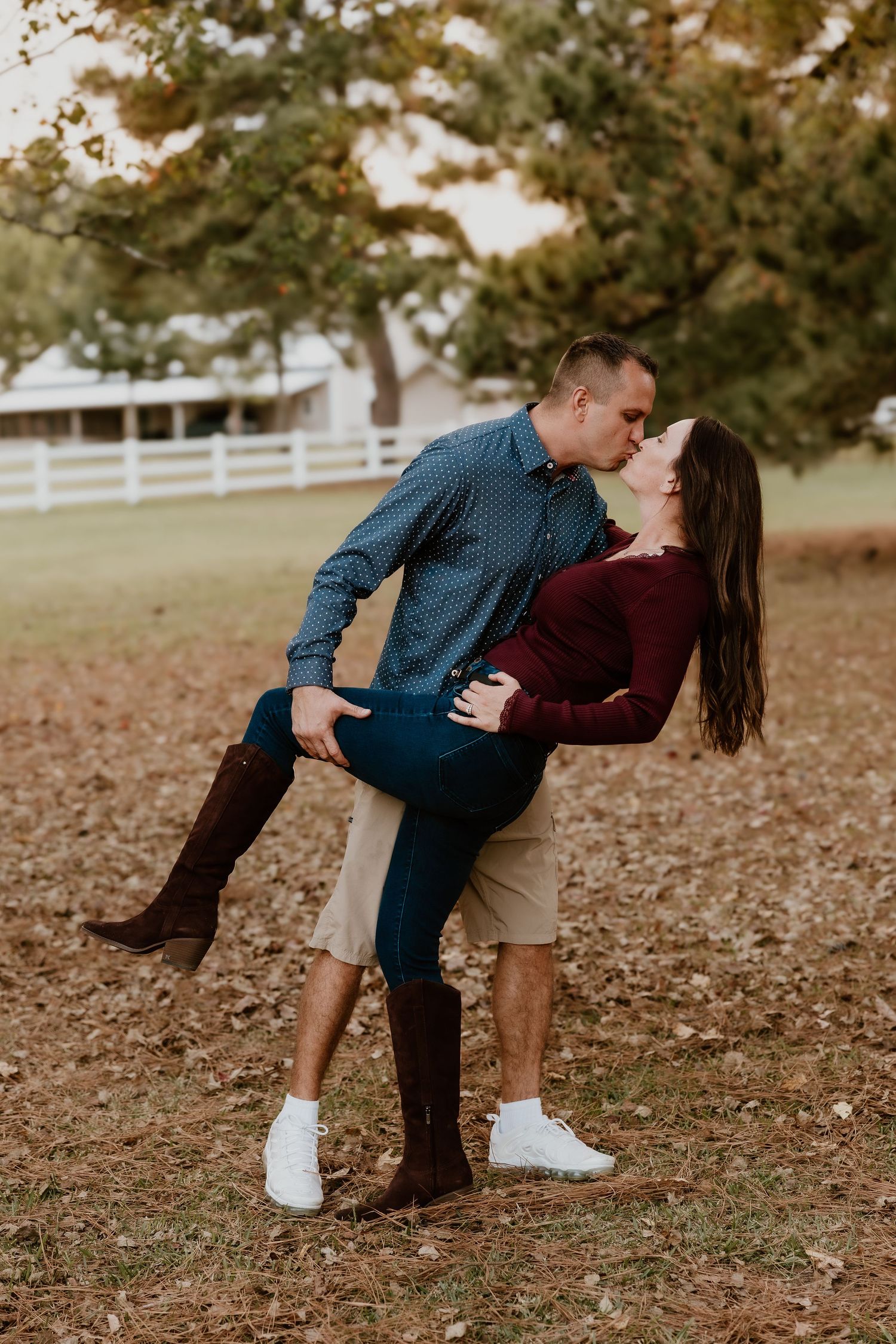 A romantic couple shares a passionate kiss while dipping in an autumn setting with fallen leaves on the ground.