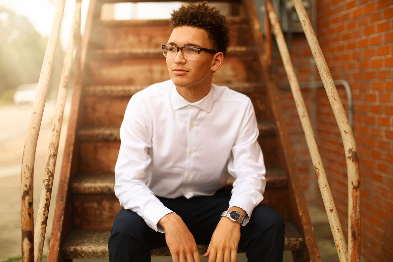 Portrait of person in white button-down shirt against industrial backdrop at golden hour.